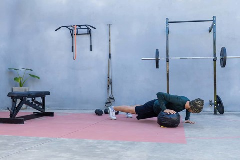 Young athlete performing push-ups with hands on a medicine ball in an outdoor gym, showcasing