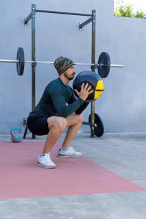 Young sportsman performing squats with a medicine ball in an outdoor gym, demonstrating strength