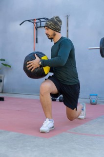 Athlete wearing a beanie, long-sleeved shirt, and shorts performs lunges while holding a medicine