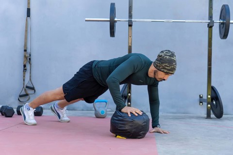 Focused athlete is doing push-ups with one hand on a medicine ball in an outdoor gym, showcasing