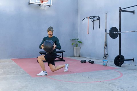 Athlete is performing lunges while holding a medicine ball in an outdoor gym, showcasing strength