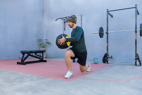 Athlete performing lunges while gripping a medicine ball in an outdoor gym, demonstrating strength