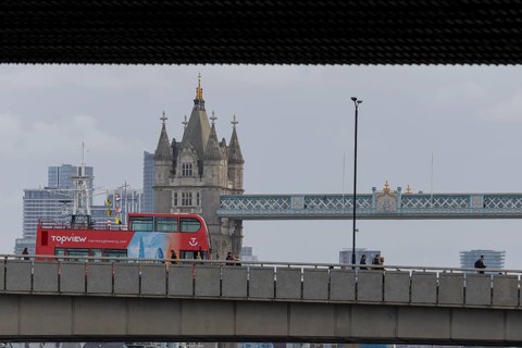 Red double decker bus driving over a bridge with Tower bridge in the background, City of London,