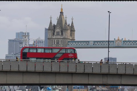 Red double decker bus driving over a bridge with Tower bridge in the background, City of London,