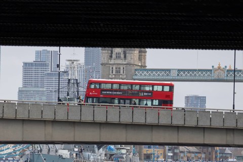 Red double decker bus driving over a bridge with Tower bridge in the background, City of London,