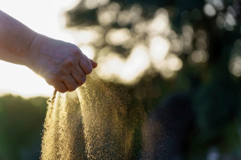 Hand pouring sand with sunset bokeh in the background, representing the passage of time