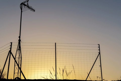 Silhouette of a television antenna and a wire mesh fence against a vibrant sunset sky