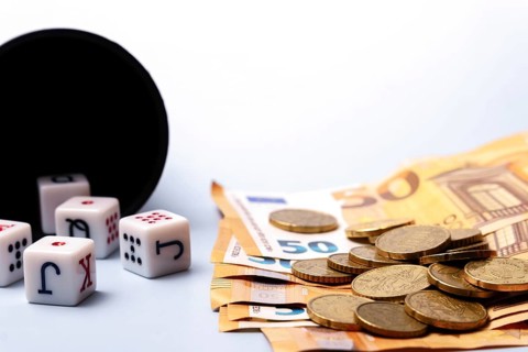 White dice with black letters and red dots are falling from a black dice cup, lying near some 50