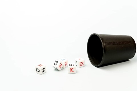 White poker dice with red and black markings rolling out of dark brown dice cup on white background