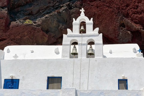 Agios Nikolaos Mavrorachidi, chapel with bell tower in front of red rock face, volcanic rock,