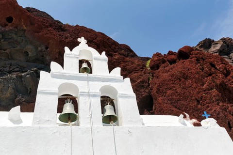 Agios Nikolaos Mavrorachidi, chapel with bell tower in front of red rock face, volcanic rock,