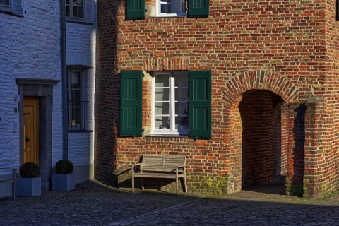 Red brick house with green shutters and bench in the shade, DÃ¼sseldorf