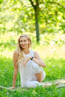 A woman dressed in white sits gracefully on a mat in a lush park, surrounded by vibrant green grass