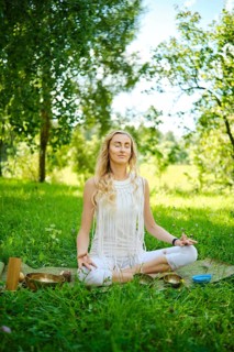 A woman peacefully meditates on a mat in a vibrant green park, surrounded by trees and nature