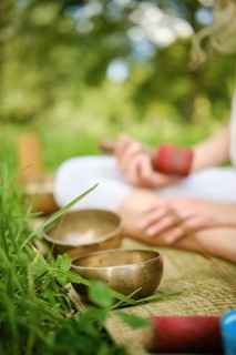 Participants are engaged in a peaceful outdoor meditation session, skillfully playing singing bowls