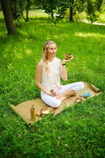 A woman engages in a calming meditation session, holding a singing bowl while seated on a mat in a