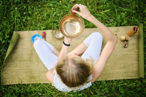 Overhead view of a woman sitting cross-legged on a mat, skillfully playing a singing bowl.