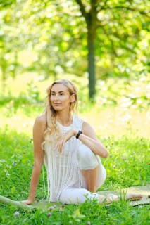 A woman with long hair sits elegantly in a vibrant green park. Dressed in white, she poses