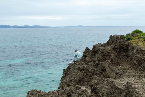 Angler at Sesoko's tail, rock formation, rugged cliffs of volcanic rock at the southern tip of
