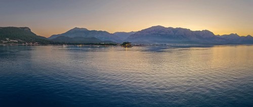 Panoramic dusk scene in Kemer, Turkey, showing the town illuminated coastline and beach, reflected