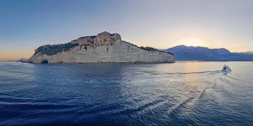 Vibrant evening seascape with a boat cruising away on the blue sea, near the Pirate Cave in Kemer