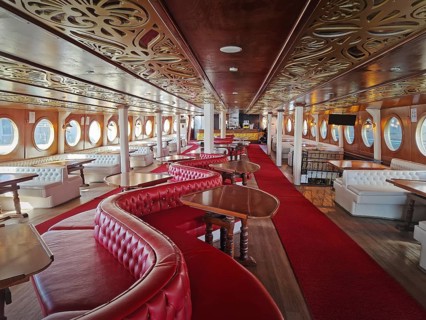 Luxurious ship interior with long hall, red carpets, leather couches and curved wooden tables.