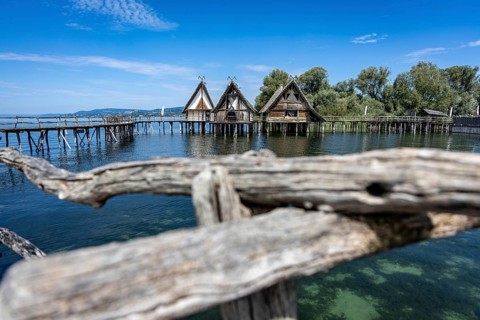 Pile dwellings protrude into the water, embedded in a picturesque lake and hilly landscape,