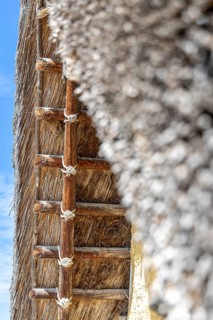 Close-up of a thatched roof with rope connections against a blue sky, pile dwellings at