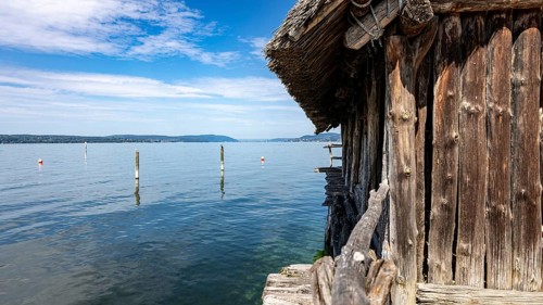 Wooden hut directly on the lake with blue sky and scattered clouds, pile dwellings Unteruhldingen