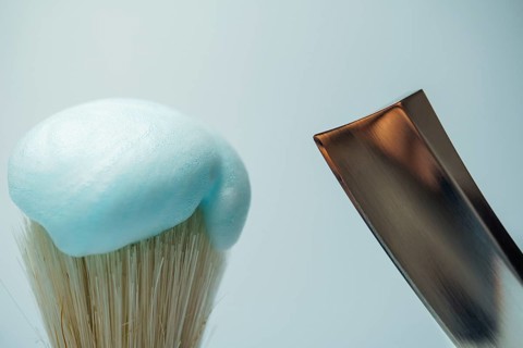 Shaving brush with light blue foam and metal razor blade ready for skincare routine