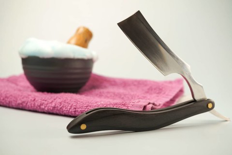 Shaving accessories including a straight razor, shaving soap, and pink towel evoke a sense of