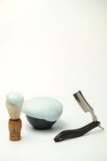 Shaving foam in a bowl, shaving brush and a straight razor are arranged on a white background,