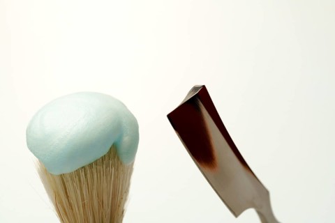 Shaving brush with light blue foam and straight razor on white background, getting ready for