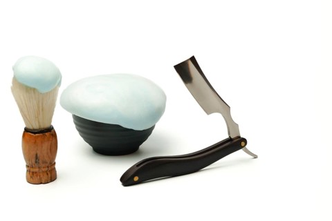 Shaving foam, brush, and straight razor are creating a grooming still life on a white background