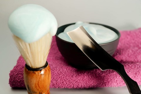 Shaving brush, razor and shaving cream resting on pink towel
