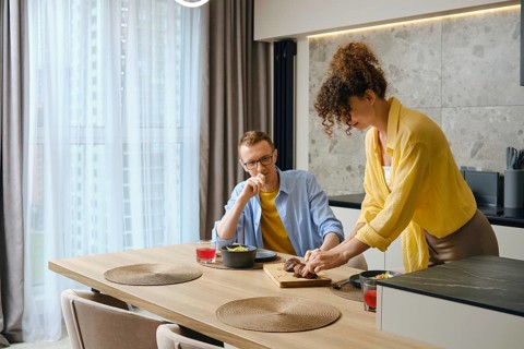 A man and woman are preparing a meal together in a modern kitchen. The woman slices food on a