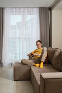 A man sits comfortably on a stylish couch in a contemporary apartment. He is focused on his