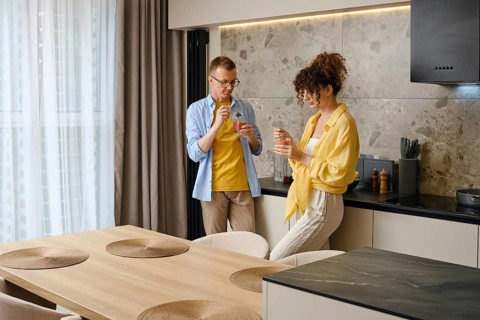 Couple eating a fruit smoothie while standing in the kitchen. The stylish space features a wooden