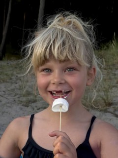 Happy blonde 7 year old Scandinavian girl eating marshmallows outdoors in Ystad, SkÃ¥ne County,