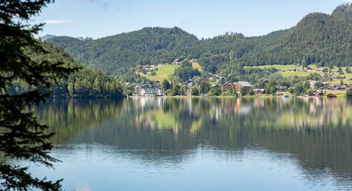 Tranquil lake with surrounding village and wooded hills on the shore reflected in the water,