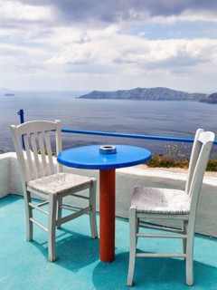 Blue table and two white wooden chairs on a terrace with sea view, typical view of the volcanic