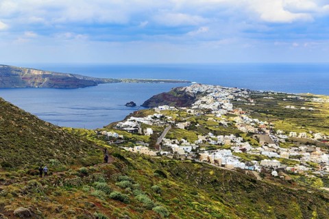 Coastline with view of the village of Oia, hiker on hiking trail from Fira to Oia, Thira,