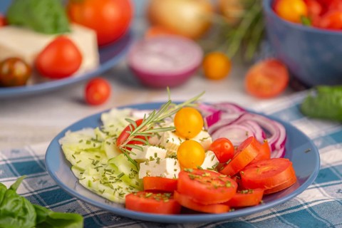 Tomatoes, cucumber, onion and feta on a plate, surrounded by vegetables and herbs