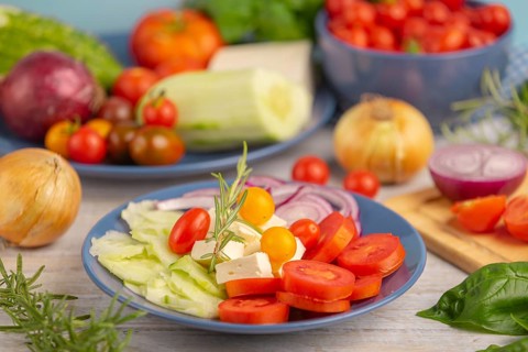Tomatoes, cucumber, onion and feta on a plate, surrounded by vegetables and herbs