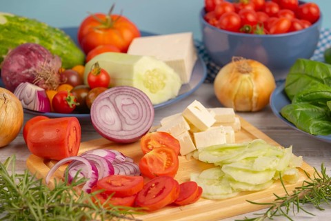 Fresh and sliced vegetables with feta on a wooden board, surrounded by basil and rosemary, rustic