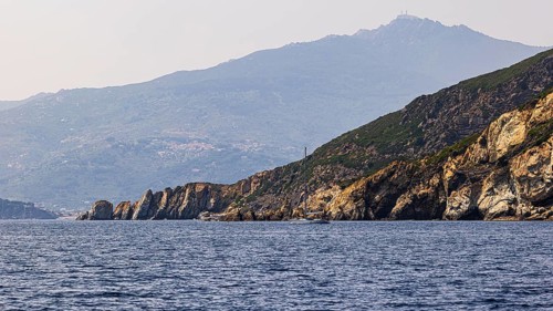 Rocky cliffs near Marina di Campo, in the background in the haze the peak of Monte Capanne, Elba