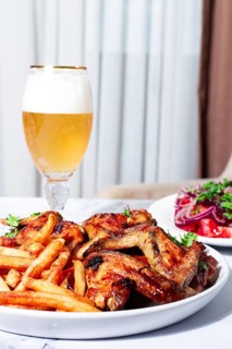 Delicious barbecue chicken wings, with French fries, salad and a refreshing drink, at a cozy table,