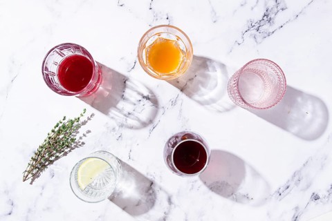 An assortment of drinks on a marble surface, with fresh greenery and shadows, in natural light, top