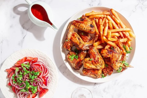 Delicious barbecue chicken wings, with French fries, salad and a refreshing drink, at a cozy table,
