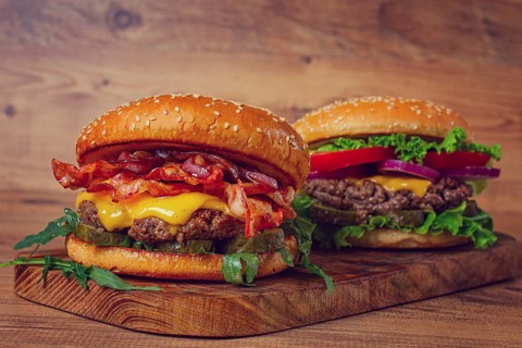 Two burgers with beef patty, fried bacon, cheddar cheese, tomatoes, homemade, no people